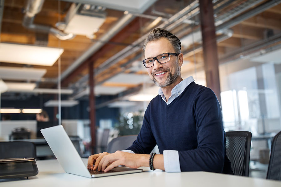Mature businessman sitting at table with laptop. Manager working on laptop computer in mod