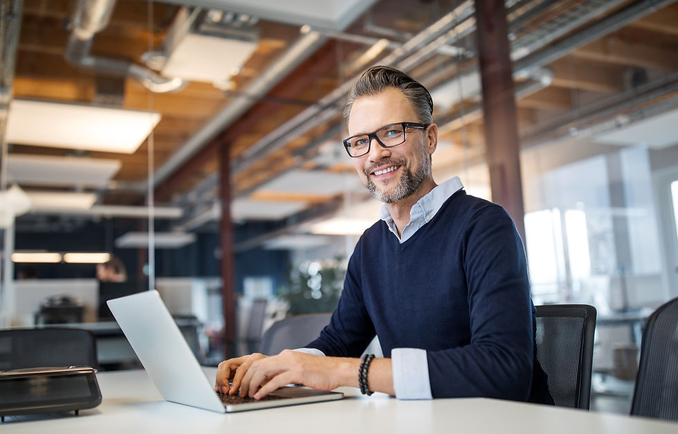 Middle-aged man with glasses smiling while working on laptop in office