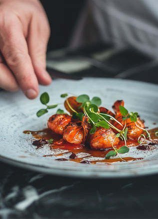 Hand garnishing a plate of grilled seafood with microgreens.