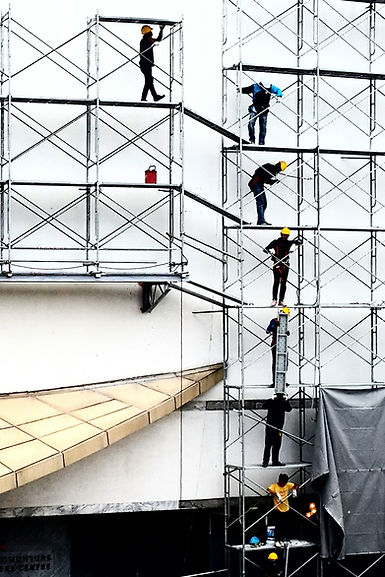 Workers standing on multi-level safety scaffolding attached to a white building wall