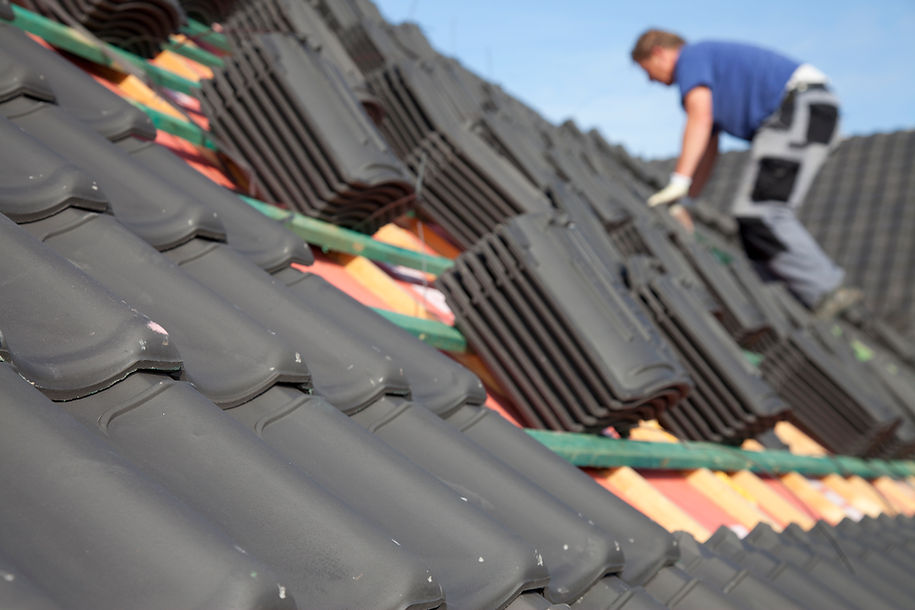 Man working on the roof with lots of black plastic tiles
