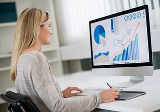 Woman sitting at a desk while analysing a desktop monitor displaying financial graphs