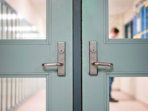 Close-up of mint green double doors with silver handles in a quiet hallway, with blurred lockers and a person in the background