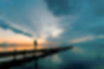 Young woman standing lakeside on jetty having a look at magical cloudscape and sunset