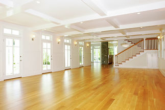 Spacious, well-lit room with wooden flooring, large windows, and a staircase