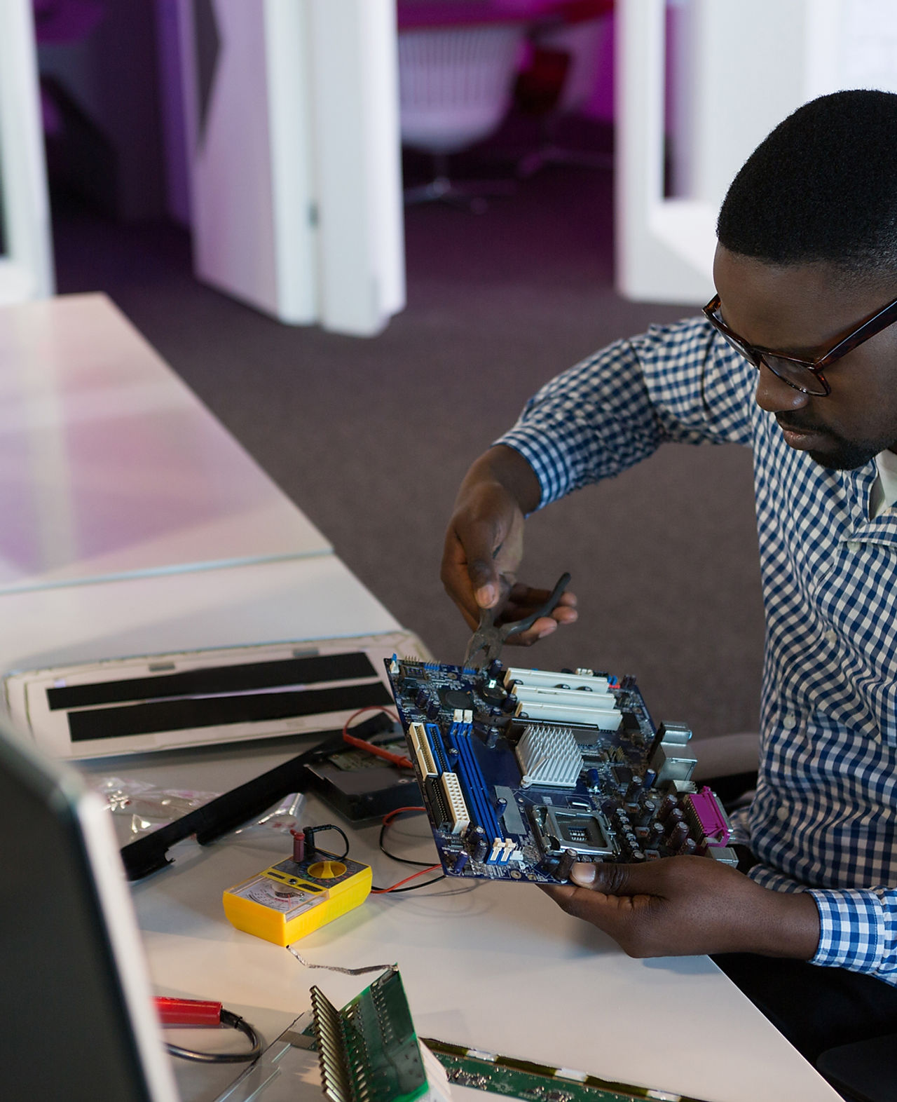 A man sitting at a desk, repairing a computer motherboard.