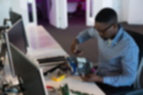 A man sitting at a desk, repairing a computer motherboard.