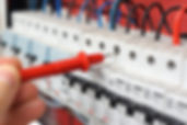 Hand of an electrician with multimeter probe at an electrical switchgear cabinet