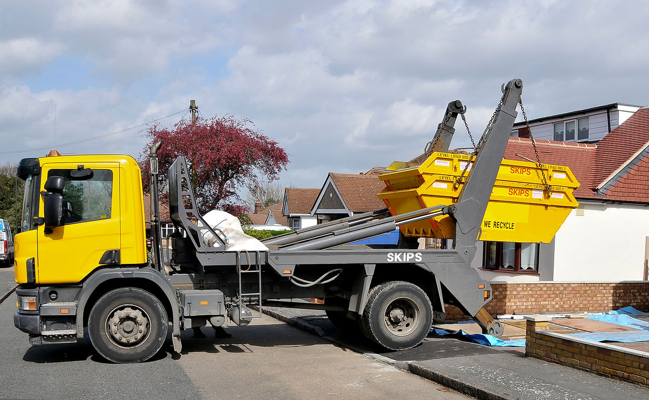 A yellow and black truck with a skip attached parked outside the residential street