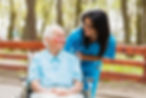 Nurse and elderly lady in wheelchair chatting outdoors