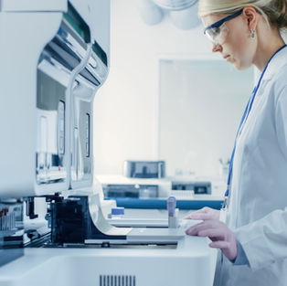 Scientist in lab coat using advanced equipment in a bright laboratory. She wears safety goggles and focuses on her work.
