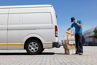 Delivery man standing behind a courier van on phone with a stack on boxes and parcels