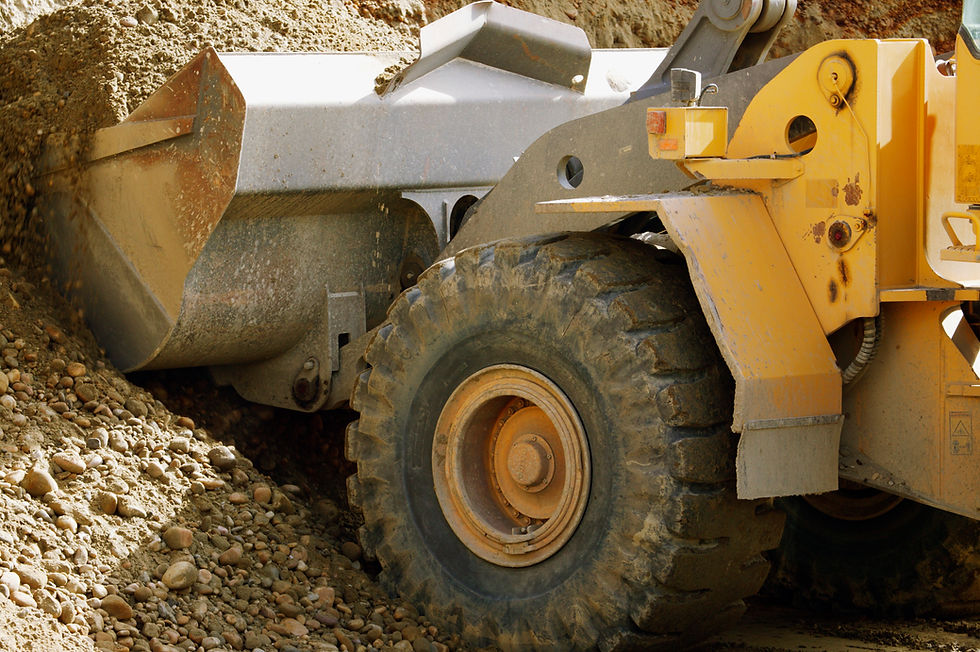 Close-up of a yellow loader bucket discharging gravel next to a large off-road tyre