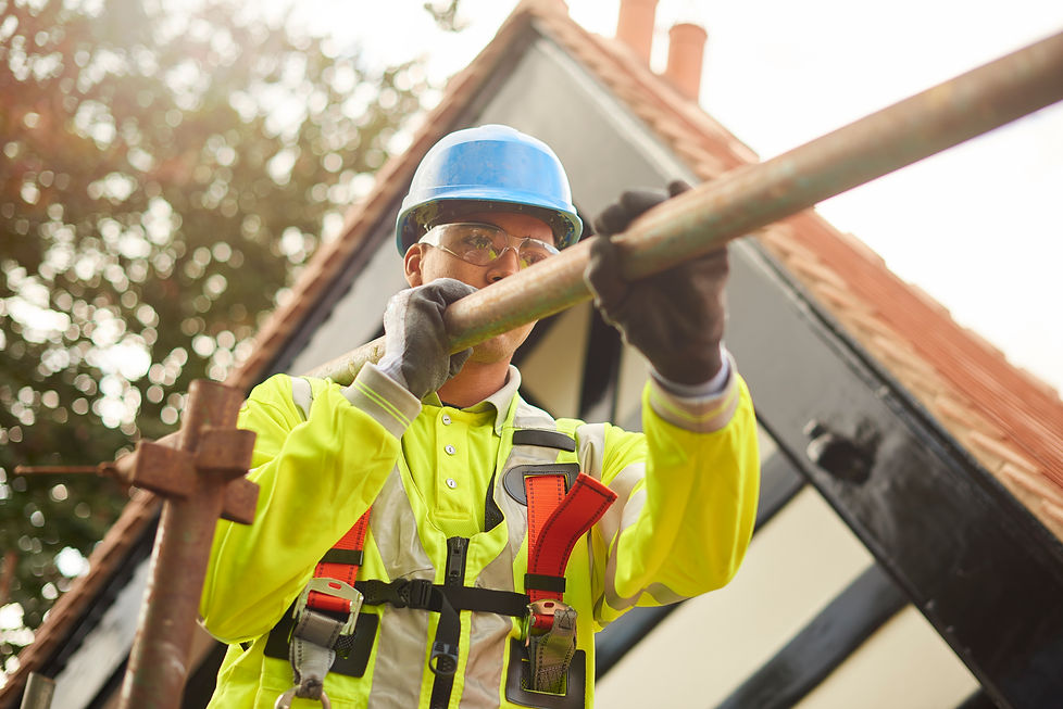 A construction worker in a safety helmet and high-visibility jacket handles scaffolding