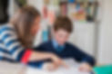 A teacher leads a student as they are both engaged in the lesson and the teacher providing assistance.