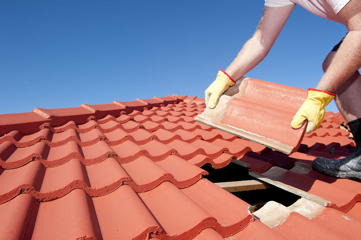 Roof repair, worker with yellow gloves replacing red tiles or shingles on a house