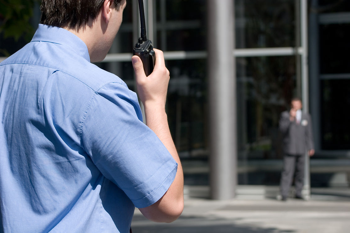 two security guards communicate by walkie-talkie in front of building