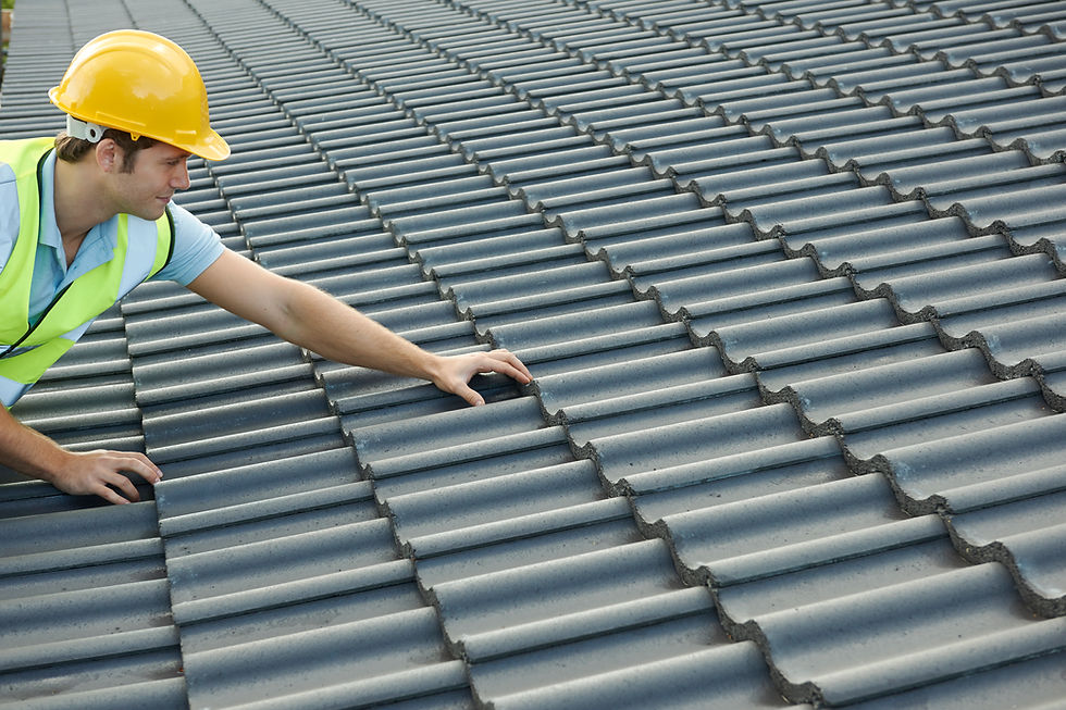 Roofer inspecting grey concrete roof tiles while wearing a yellow hard hat