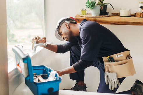 African male plumber looking at leaking bathroom tap. Professional handyman trying to fix