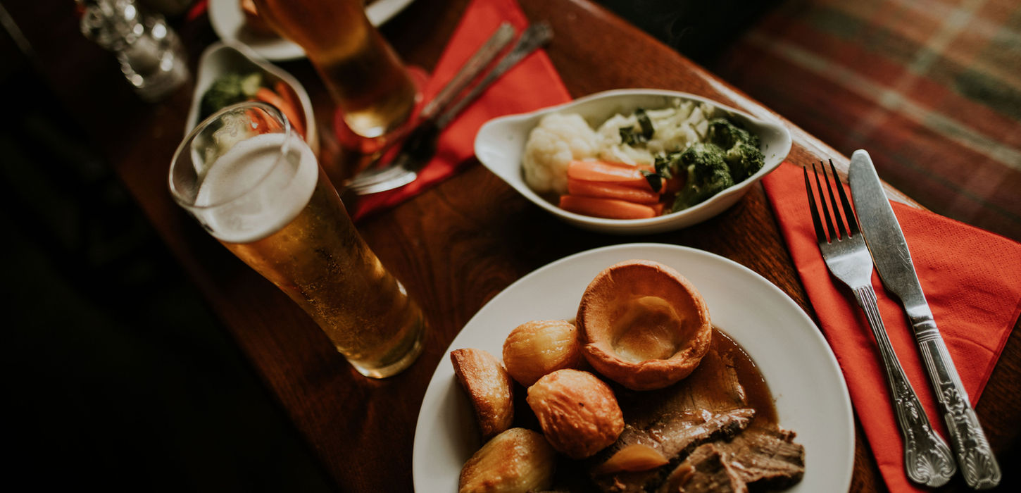 Roast dinner with meat, potatoes, vegetables, and two beers