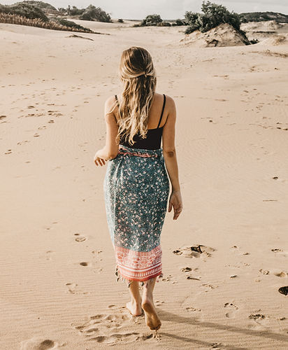 Moça de saída de banho, caminhando na praia sobre a areia.