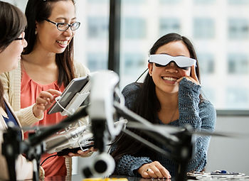 Two smiling women looking at another woman who is wearing VR glasses.