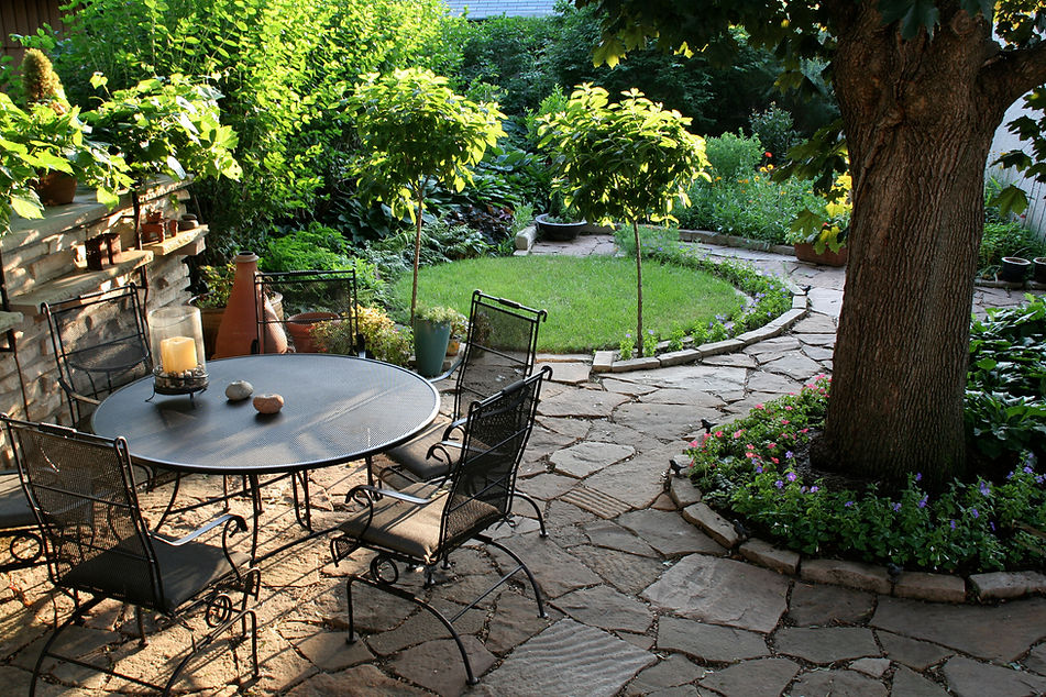 Sunlit garden patio with a round table and wrought iron chairs on a stone path