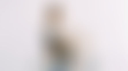 Woman standing in a bright, minimal room holding and looking at a gift box she has just received.