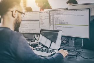 A person works on a laptop with multiple monitors