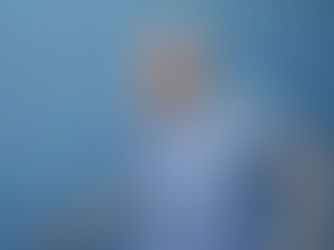 A joyful individual with vibrant blue eye makeup and a textured blue dress beams with happiness against a matching blue backdrop.