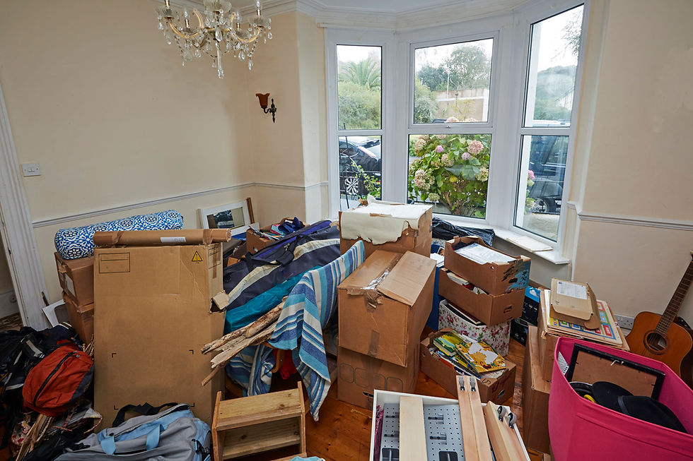 A domestic room heavily filled with packing boxes, storage containers, and personal belongings
