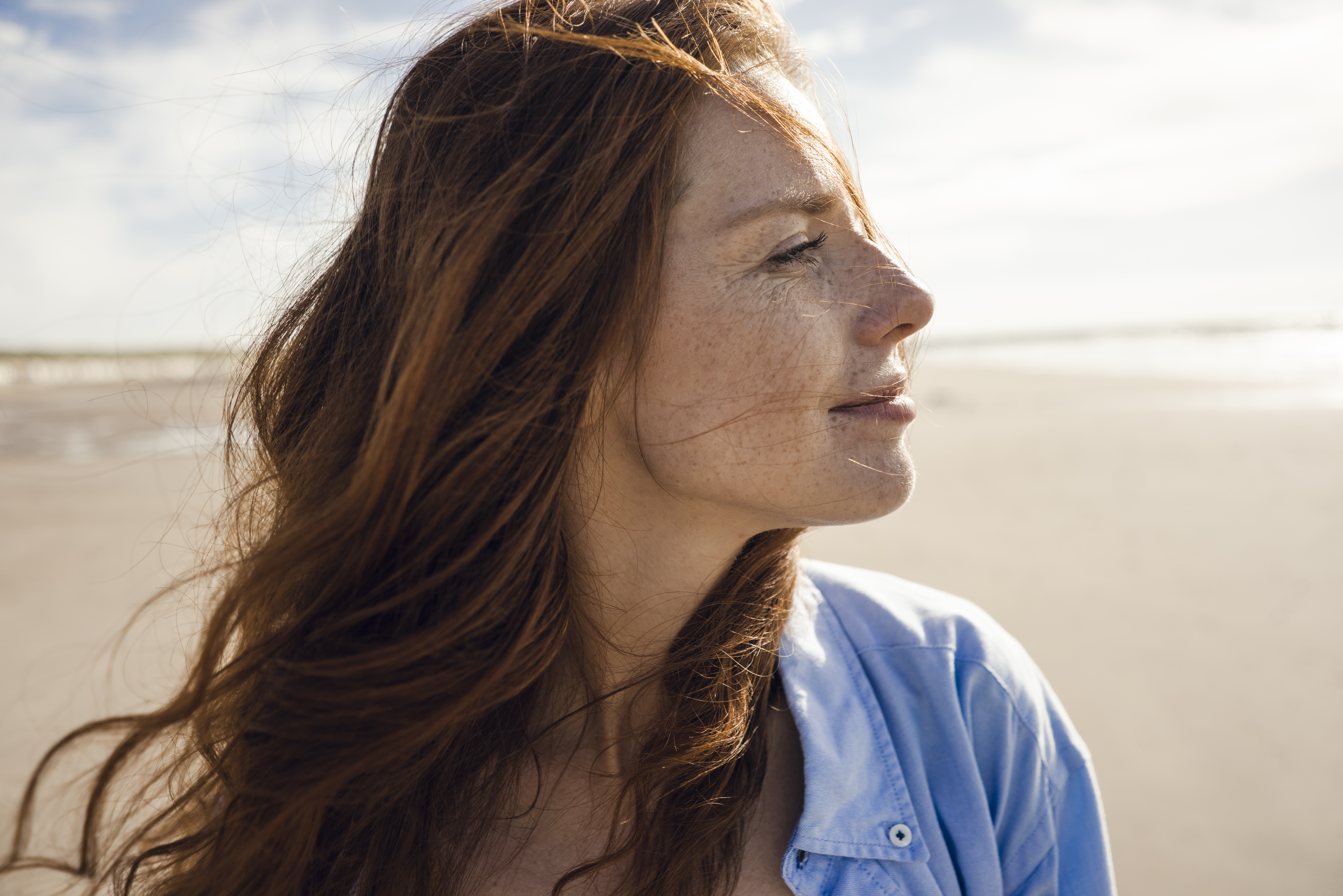 Woman with red hair, at the beach, side profile, looking at the water