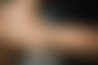 Close-up of a wrist wearing a gold bracelet with sparkling gemstones, against a blurred dark background, highlighting the jewelry's elegance.