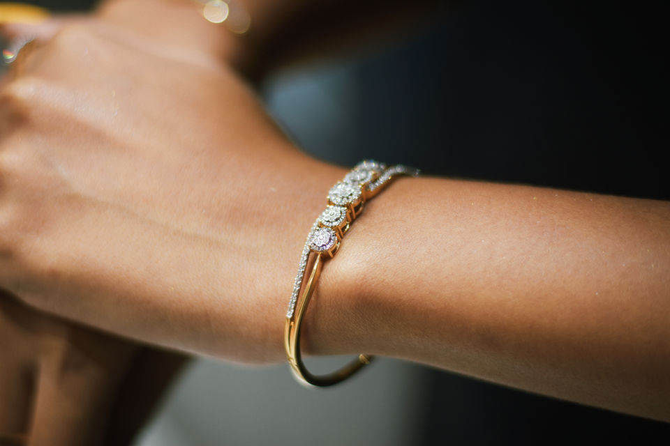 A woman wearing an openable diamond kada, featuring round brilliant cut diamonds, in yellow gold.