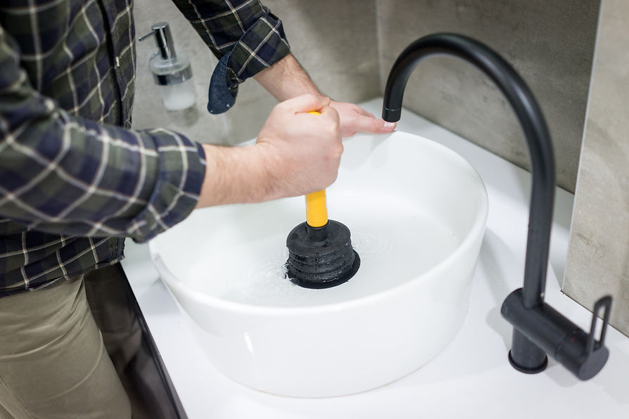 Plumber using a black and yellow plunger to unblock a white bathroom sink with a modern black faucet