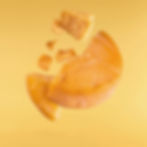 Bitto Aged cheese wheel breaking into chunks mid-air on a yellow background, showcasing texture and vibrant orange hues.