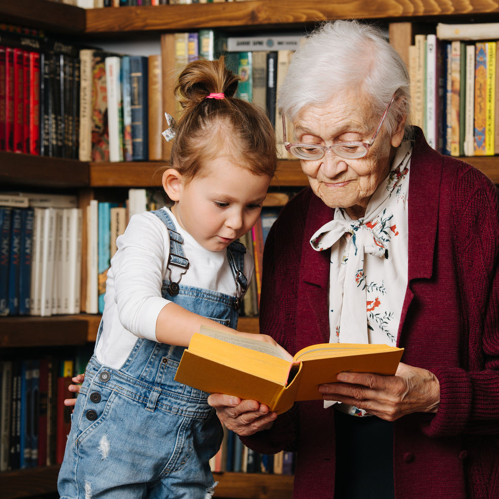 Elderly woman and little girl reading a yellow book in library.