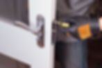 Gloved hand using a screwdriver to adjust a metal door lock on a white door
