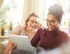 a female same sex couple sit on the sofa on their digital tablet doing some online shopping
