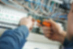 Electrician in blue uniform uses a screwdriver to adjust wiring in a circuit breaker panel
