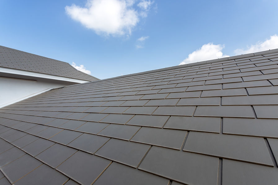 A roof with neatly arranged gray tiles stretches upward against a bright blue sky