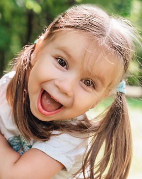 A smiling girl with pigtails leans into frame