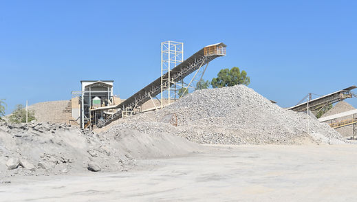 Industrial conveyor belt piling crushed limestone at a quarry and crushing plant under a clear blue sky