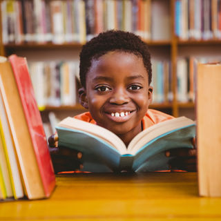 child smiling in a library while reading a book