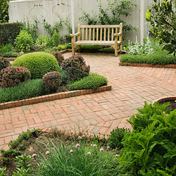 Urban small garden with brick patio, wooden bench and potted plants