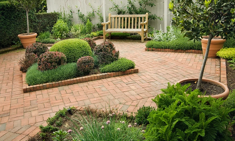 Urban small garden with brick patio, wooden bench and potted plants