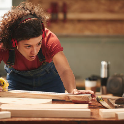 Frau, welche Maß an einem Holzbalken nimmt.