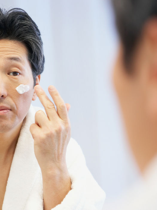 Man applying face cream in bathroom mirror