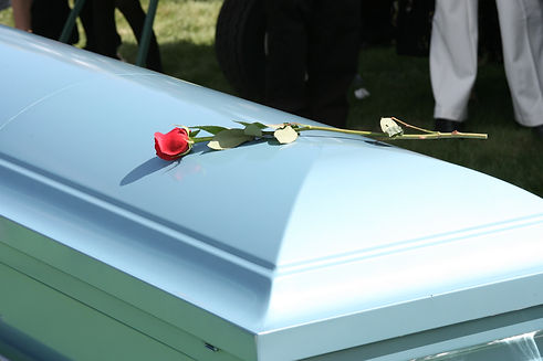 A light blue coffin adorned with a single red rose, set outdoors on grass