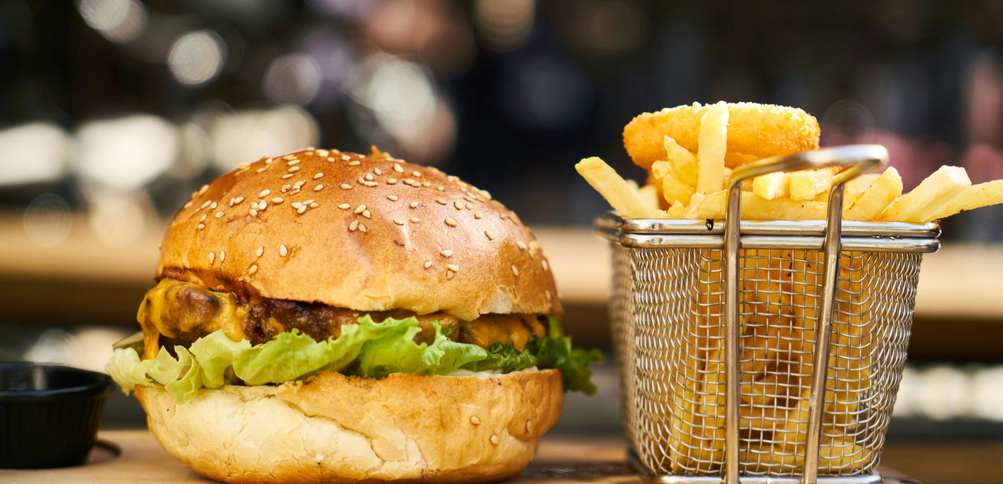 Hamburger with lettuce, fries, and onion rings on a board